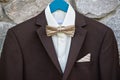 Elegant brown male tuxedo with white shirt and bow tie hanging on stone wall outdoors, copy space. Modern men accessories. Royalty Free Stock Photo