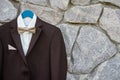 Elegant brown male tuxedo with white shirt and bow tie hanging on stone wall outdoors, copy space. Modern men accessories. Royalty Free Stock Photo