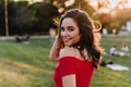 Elegant brunette girl posing in park in summer day. Blithesome young lady in red dress enjoying natu