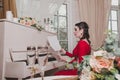 Elegant brunette 30-35 year old woman pianist in evening red dress sits at the retro piano, looking on musical notes in Royalty Free Stock Photo