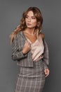 Elegant business lady in the checkered suit and satin blouse looking aside and posing on the gray background, .