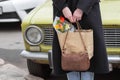 Business woman in black vintage coat holding retro leather handbag and shopping bag with flowers. Retro car background. Royalty Free Stock Photo