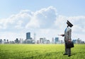 Camera headed man standing on green grass against modern cityscape