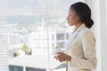 Elegant businesswoman with tea cup looking through office window