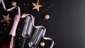 Elegant Christmas composition with rose wine bottle, champagne glasses, balls decorations, stars, confetti on black background. Royalty Free Stock Photo