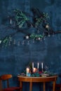 Elegant Christmas table setting with cozy candles, plates, pomegranate and branch of fir tree. Vintage blue wall copy Royalty Free Stock Photo