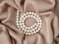 Glimmer of natural pearl beads necklace on abstract beige knitted fabric background. Pearl necklace on a delicate rose