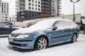 Classic blue car Saab Aero covered with snow during snowfall in harsh winter