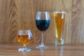 Composition of alcoholic drinks with glass of whiskey, glass of clear beer and glass of red wine on stage of oak tables
