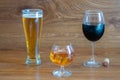 Composition of alcoholic drinks with glass of whiskey, glass of clear beer and glass of red wine on stage of oak tables
