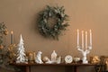 Elegant composition of christmas living room interior with wooden console, stylish wreath, deer candlestick with candle, clock,