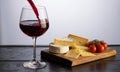 Red Wine Being Poured Near Cheese Assortment And Fresh Tomatoes on Wooden Board Against Bright Neutral Background Studio Shot Royalty Free Stock Photo