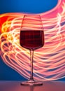 Elegant crystal glass filled with red wine on a blue background painted with colorful light. Light reflections and refractions, Royalty Free Stock Photo