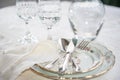 Elegant dinner set with silver knife, fork and spoon lying across luxyry porcelain dishes, and crystal glassware on cream vintage Royalty Free Stock Photo