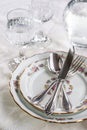 Elegant dinner set with silver knife, fork and spoon lying across luxyry porcelain dishes, and crystal glassware on cream vintage Royalty Free Stock Photo