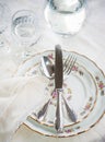 Elegant dinner set with silver knife, fork and spoon lying across luxyry porcelain dishes, and crystal glassware on cream vintage Royalty Free Stock Photo