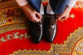 Elegant dressed man tying stylish leather shoes indoors standing on fancy oriental style carpet Royalty Free Stock Photo