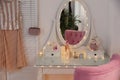 Elegant dressing table with lights and pink chair in room interior