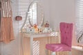 Elegant dressing table with lights and pink chair in room interior