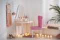 Elegant dressing table with lights and pink chair in room interior