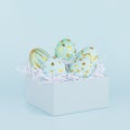 Elegant easter eggs with gold design in gift box on blue background, square.