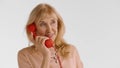 Elegant elderly blond woman talking on red landline phone isolated on white background Royalty Free Stock Photo