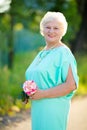 Elegant elderly woman smiling and posing with rose flower outdoors Royalty Free Stock Photo