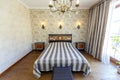 Elegant expensive bedroom with a large white bed with a striped bedspread. A high headboard with a red pattern