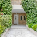 An elegant family house with stone covered walls and marble pathway between the garden to the white door.