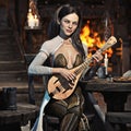 Elegant fantasy female bard plays a song in a medieval tavern with her favorite lute instrument. Royalty Free Stock Photo