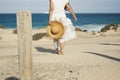 Elegant fashion lady in white dress and natural hat walking to the beach barefoot enjoying the summer holiday vacation day in Royalty Free Stock Photo