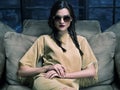 Elegant fashion model wearing mustard dress, sitting on the couch