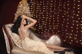 Elegant fashionable lady in golden dress lying on luxurious modern sofa over Christmas background