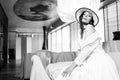 Elegant fashionable woman wearing summer white dress, straw hat, posing in stylish boho interior. Royalty Free Stock Photo