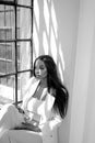 Elegant, fashionable young woman with long hair sitting near the window, relaxing during work day. Mental health and work life Royalty Free Stock Photo