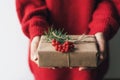 Elegant female hands holding a gift box decorated with red berries.