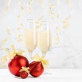 Elegant festive Christmas background with fizz champagne in glasses, shiny red balls, golden ribbon, hang curling confetti.