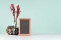 Elegant fresh home decor with red bizarre branch in black vase, decorative brown sheaf of twigs, blank photo frame in style green