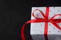 Elegant Gift Box Wrapped in Grey Silver Paper with Polka Dots Red Ribbon on Black Background. Christmas New Years Valentine Royalty Free Stock Photo