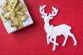 Elegant gift box wrapped in silver paper tied with golden ribbon bow white deer on dark red burgundy background. New Year Royalty Free Stock Photo