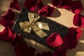 Elegant gift with a golden bow around red rose petals
