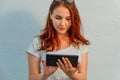Elegant ginger hair young businesswoman or student using tablet leaning to white wall, looking at screen Royalty Free Stock Photo
