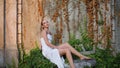 Elegant girl sitting stones in front old wall covered autumn leaves zoom in. Royalty Free Stock Photo