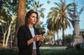 Elegant girl in suit holds a smartphone in hand and looks into distance while walking in a Park in Barcelona, girl ÃÂ¼anager checks Royalty Free Stock Photo