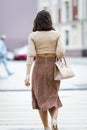 An elegant girl is walking down the street. Slim brunette in a skirt and high heels. Back view. Vertical