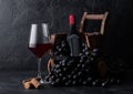 Elegant glass of red wine with dark grapes and bottle of wine inside vintage wooden barrel on black stone background. Natural Royalty Free Stock Photo