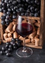 Elegant glass of red wine with dark grapes and corks inside vintage wooden box on black stone background. Natural Light Royalty Free Stock Photo