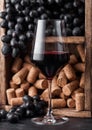 Elegant glass of red wine with dark grapes and corks inside vintage wooden box on black stone background. Natural Light Royalty Free Stock Photo