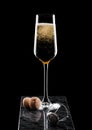 Elegant glass of yellow champagne with cork and wire cage on black marble board on black background