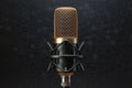 Elegant golden microphone frontally positioned on black background, podcast symbol